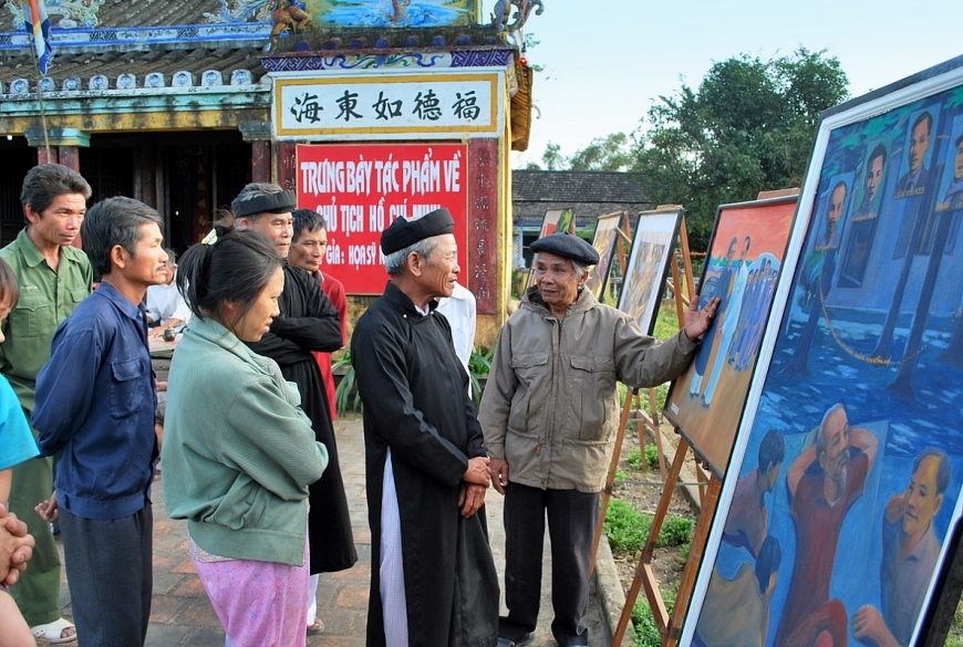 Cố họa sĩ thuyết trình từng tác phẩm vẽ về Bác Hồ cho các bô lão nghe.