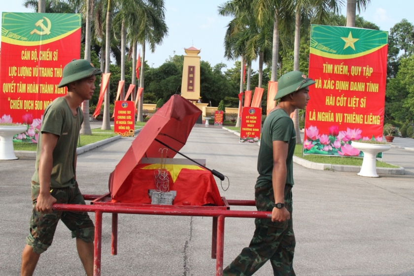Giữa trưa nắng, một chiến sĩ che ô cho hài cốt liệt sĩ sau khi khai quật, bước tiếp theo là chuyển hài cốt đến khu vực lấy mẫu xét nghiệm.