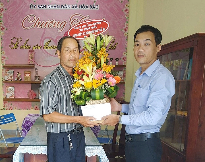 Đại diện UBND xã Hoà Bắc tặng hoa và quà cho ông Đoàn Văn Thể (trái).